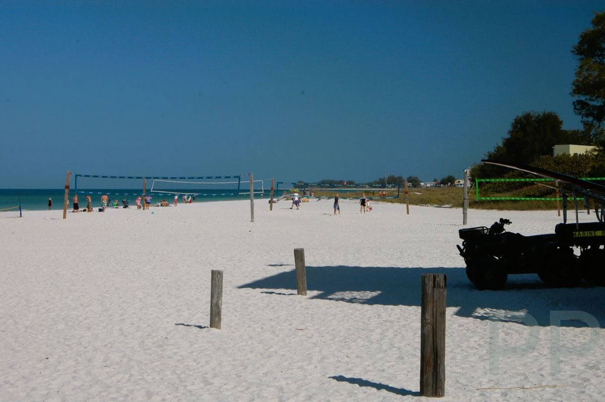 People playing beach volleyball and walking along the wide white sands of Manatee Public Beach on Anna Maria Island.